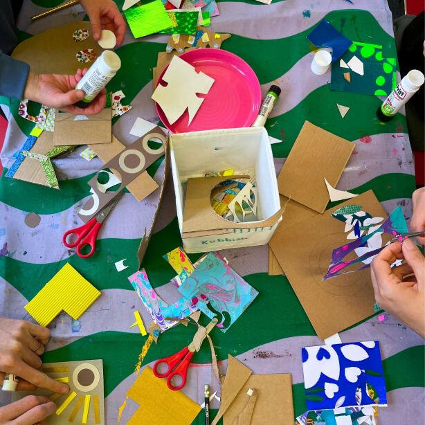 Adult and child hands creating colourful paper collage, using scissors and glue together at a bright family arts and crafts workshop in South East London