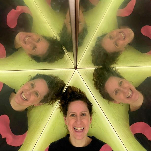 Lucie from Pattern & Print Club smiling while in a hall or mirrors with 5 of her reflecting in the mirrors