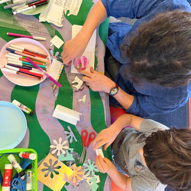Adult and child together cutting, sticking and decorating with colourful paper, bright pens and craft supplies during a family Saturday zine and art making workshop.